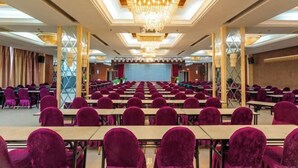 Ein Konferenzraum mit Tischen und Stühlen in Reihen, einer großen Chandelüstere und einer Bühne im Vordergrund.