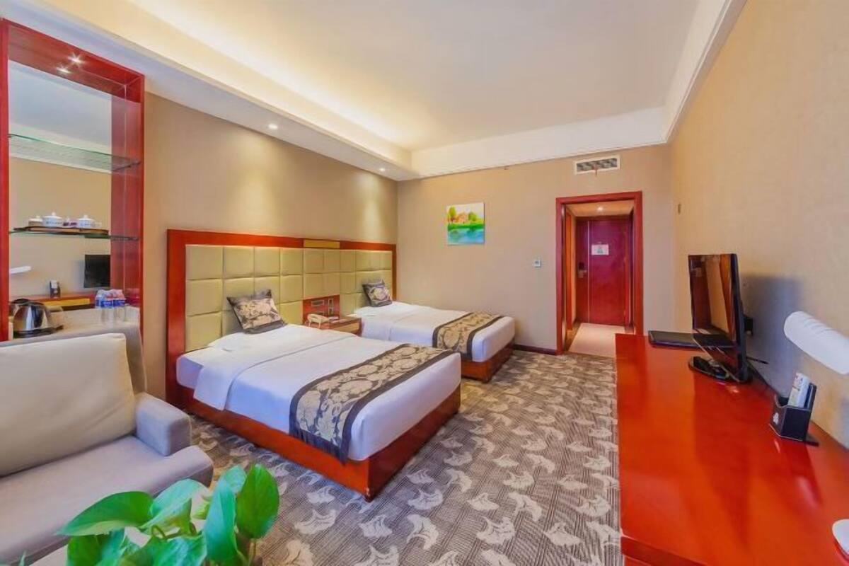 A hotel room with two beds, a sofa, a TV, and a desk.