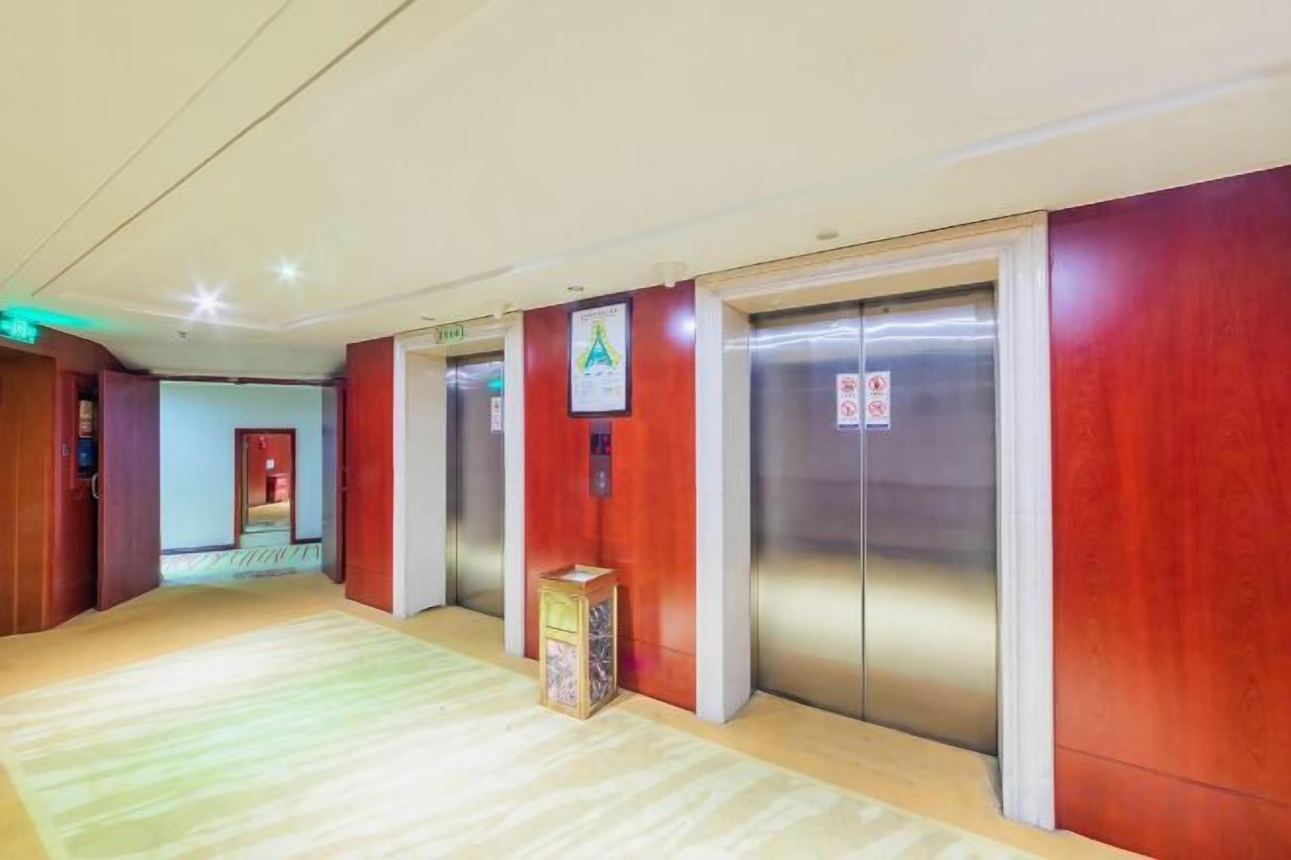 A hotel corridor with three elevators, a reception area, and a carpeted floor.