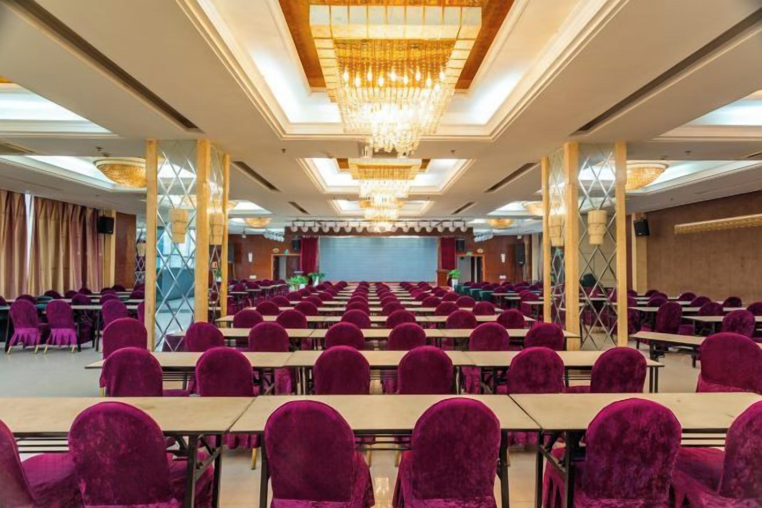 A conference room with rows of tables and chairs, a stage, and a large chandelier.