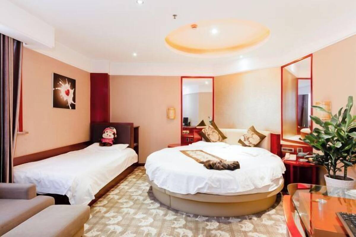 A hotel room with two beds, a desk, a chair, a mirror, and a plant.