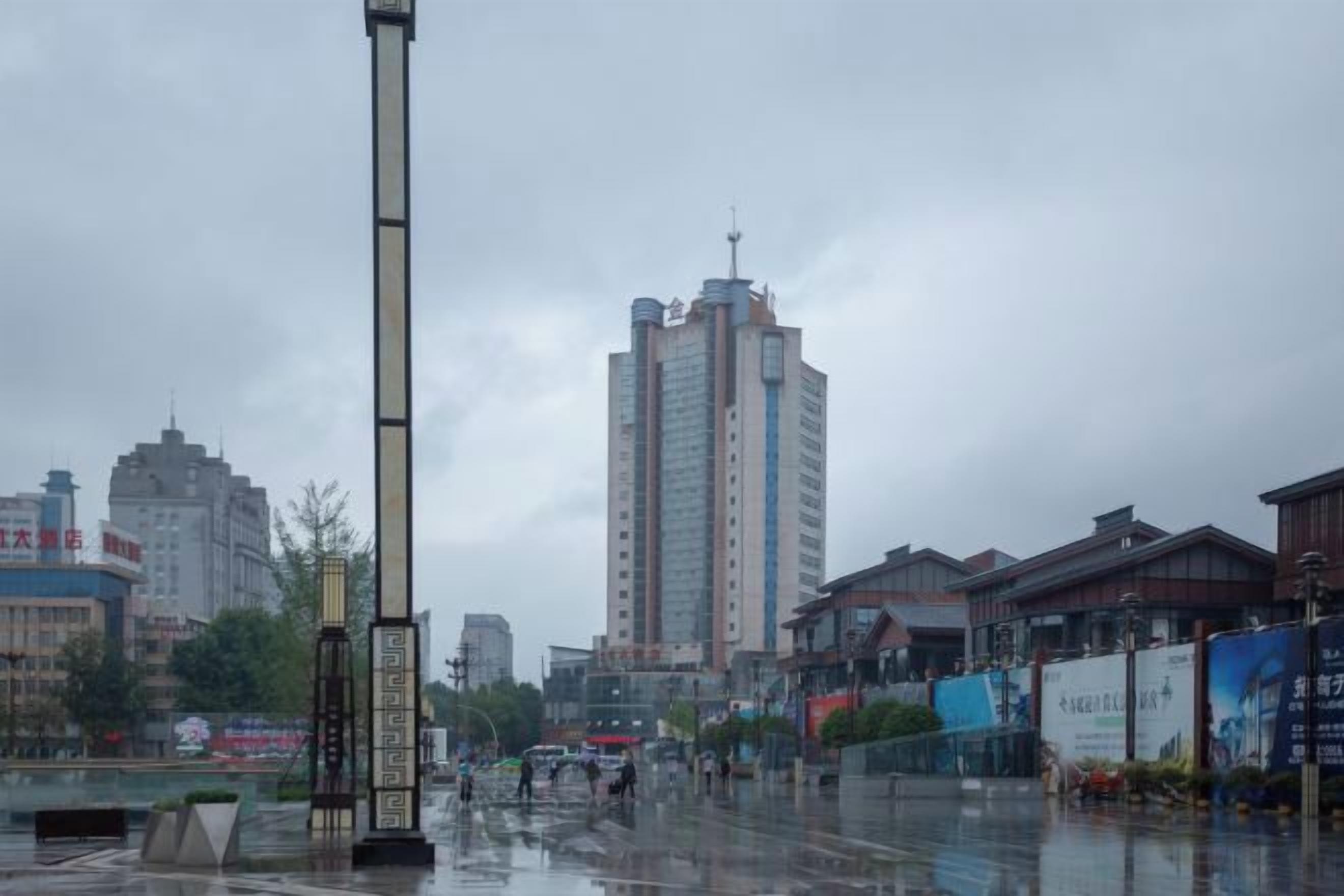 A cityscape with a tall building, wet streets, and various commercial establishments.