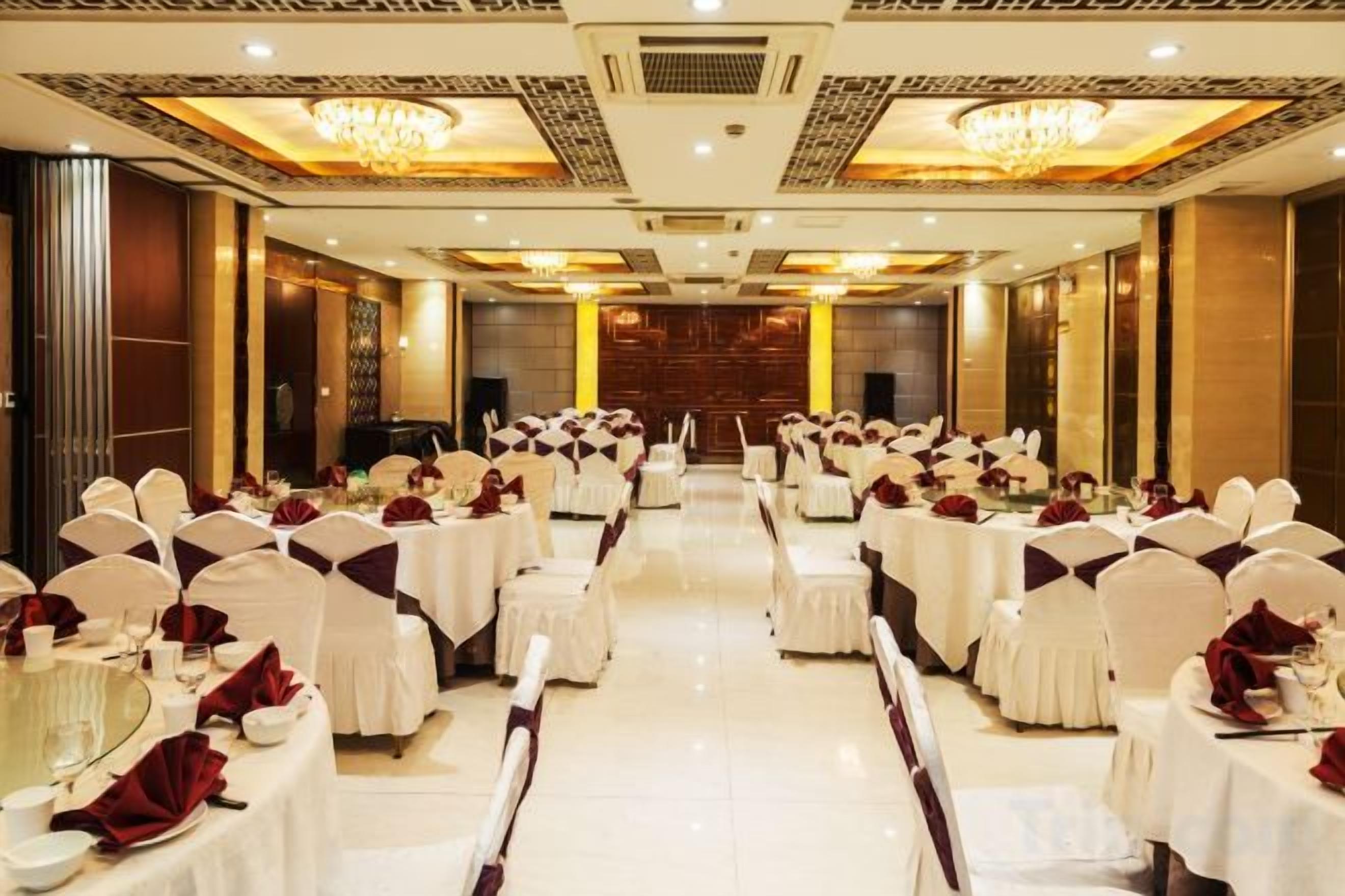 Un salón de banquetes con mesas y sillas redondas, un escenario al frente y una lámpara de araña.