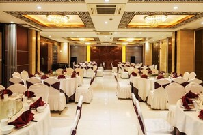 A banquet hall with round tables and chairs, a stage at the front, and a chandelier.