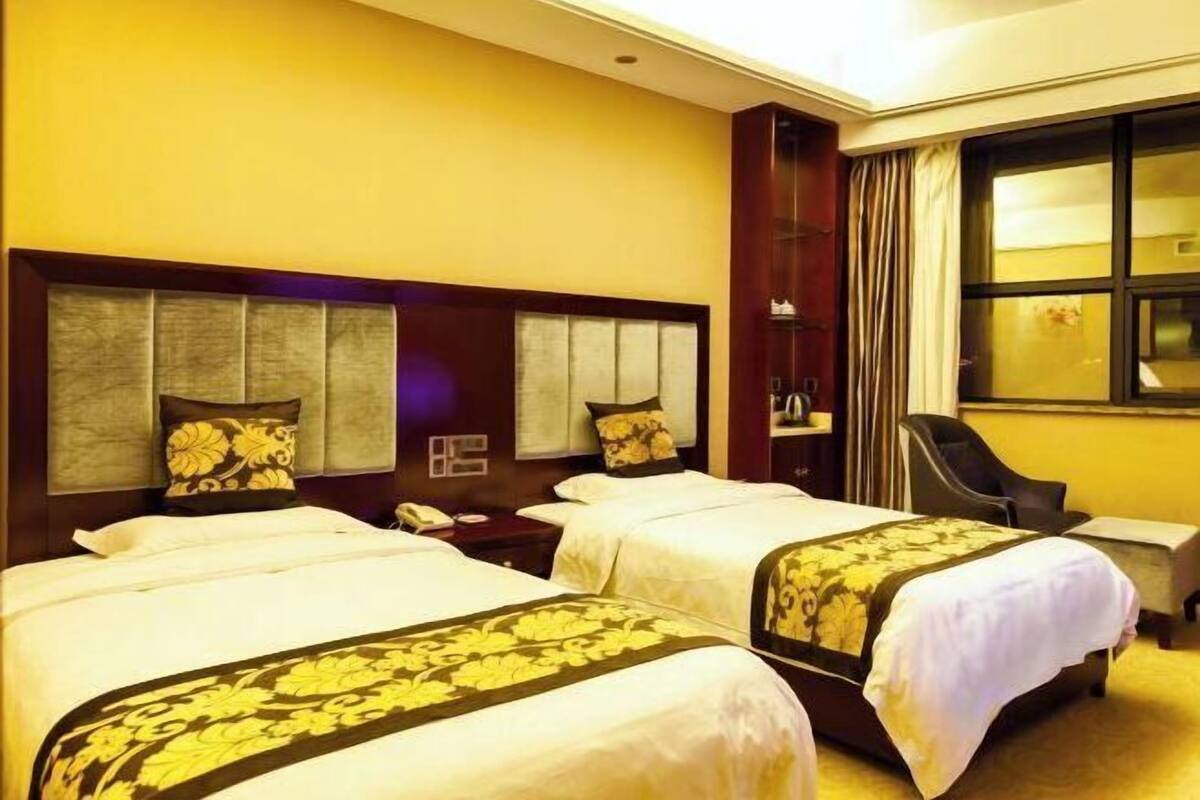 A hotel room with two beds, a nightstand, a desk, and a window with curtains.