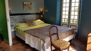 Une chambre à coucher avec un lit, une chaise, une table de chevet, une lampe et une fenêtre.
