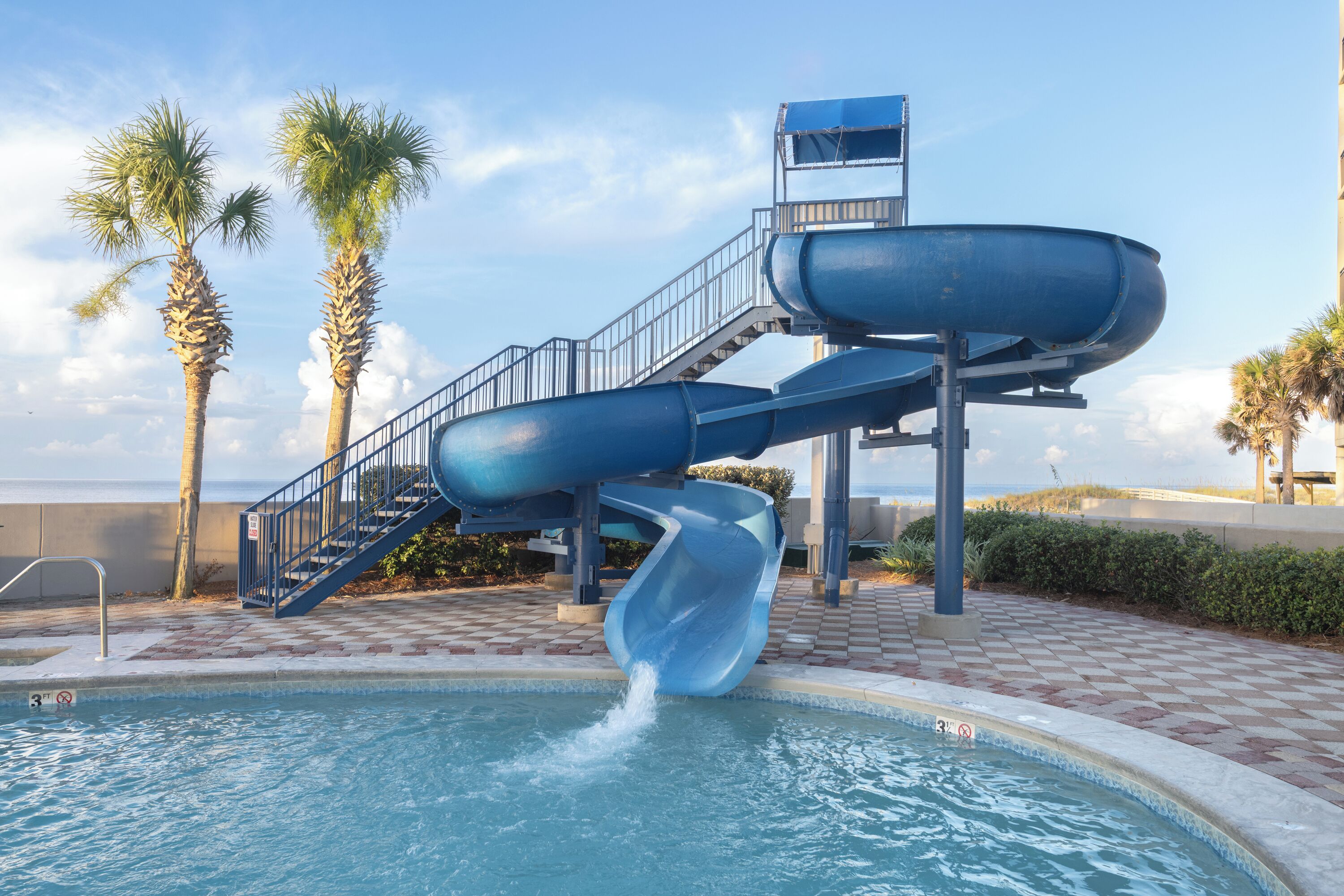 Eine Wasserrutsche über einem Pool mit Palmen und blauem Himmel.
