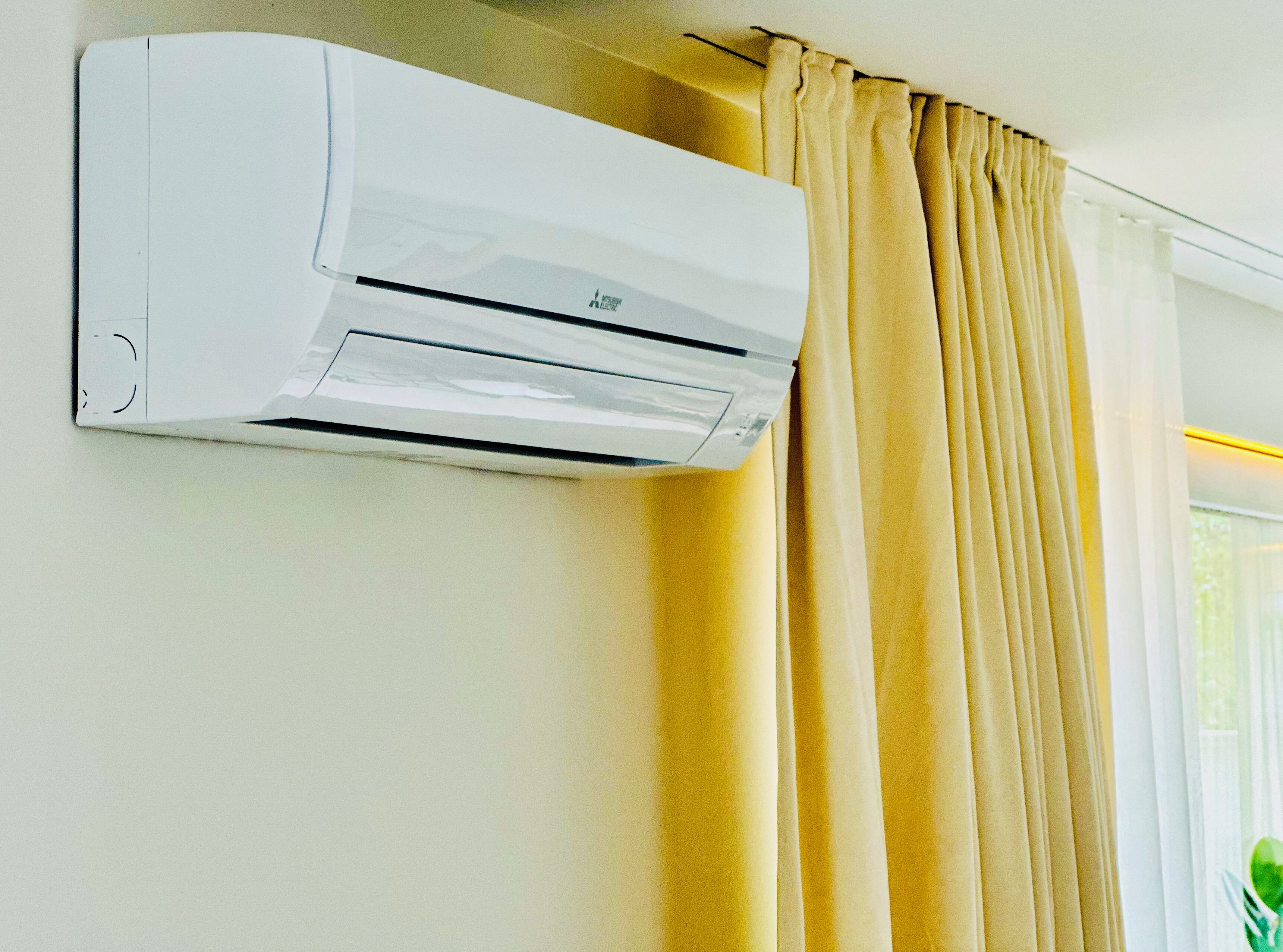 Ar condicionado fixado na parede em um quarto com janela e cortinas.
