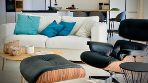 A modern living room with a sofa, black leather chairs, a wooden coffee table, and a kitchen area in the background. - Homely Basel Airport (Saint-Louis)