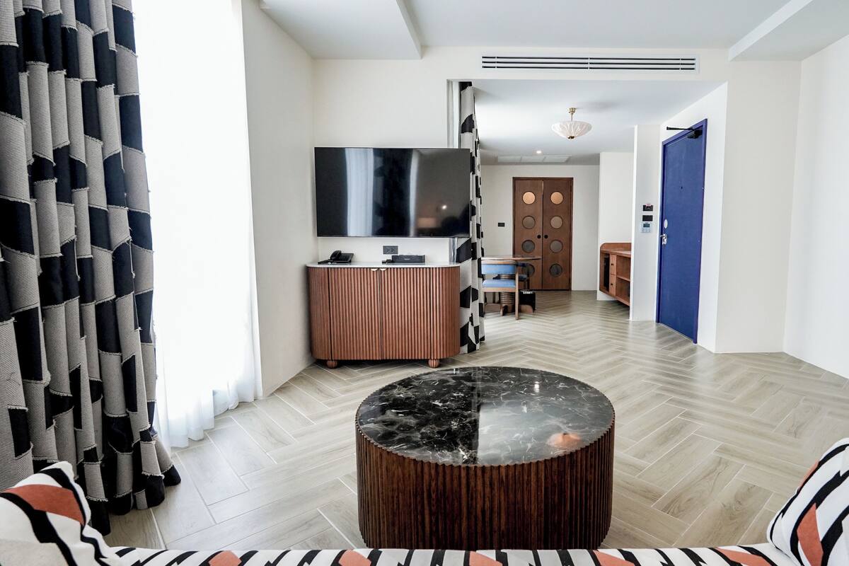 Un salon moderne avec une table basse ronde, un canapé, un téléviseur fixé au mur et un meuble en bois.