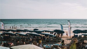 Une plage bordée de rangées de transats et de parasols, un rivage sablonneux et l’océan.