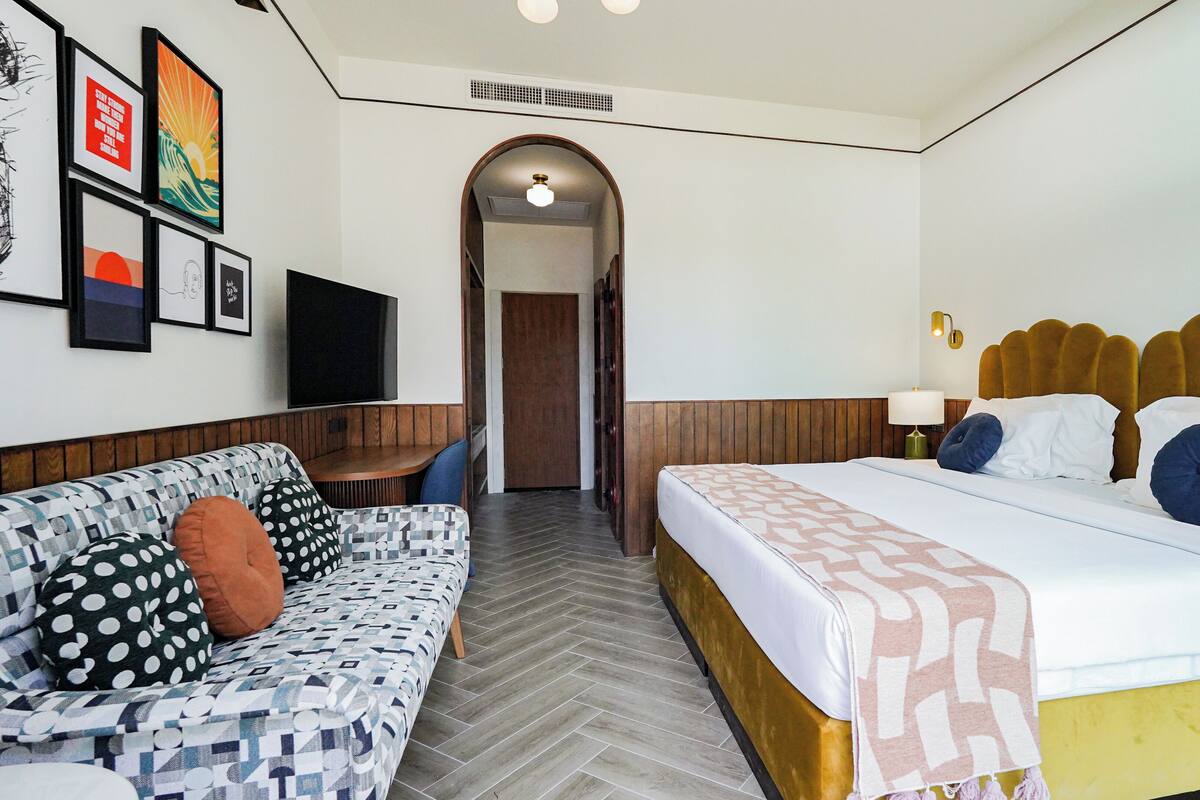 Une chambre d’hôtel avec un lit, un canapé, une télévision et des œuvres d’art encadrées accrochées au mur.