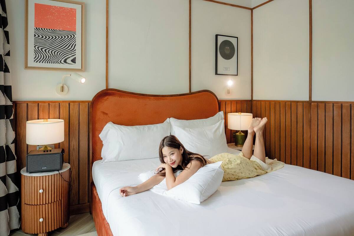 Un lit avec du linge de lit blanc, une tête de lit en bois, deux lampes de chevet et un tableau encadré au mur.