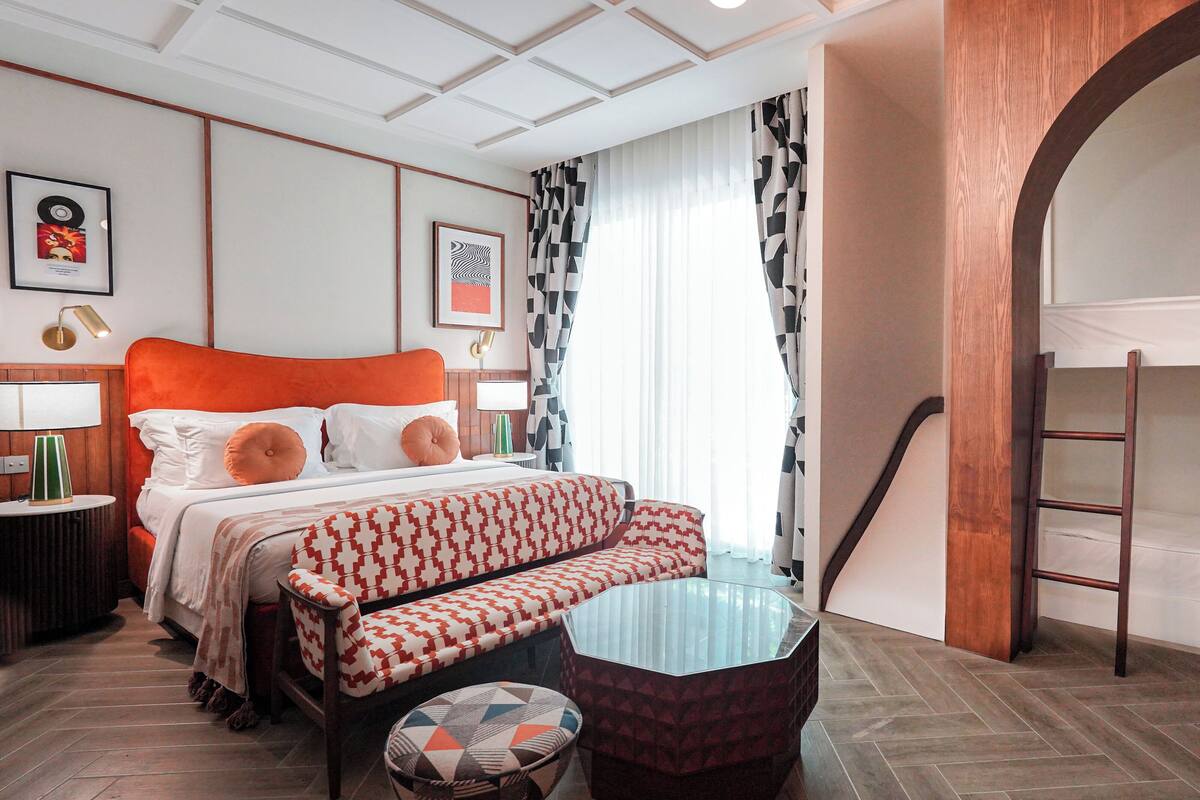 Une chambre d’hôtel avec un lit, un canapé, une petite table, une échelle et un lit superposé.