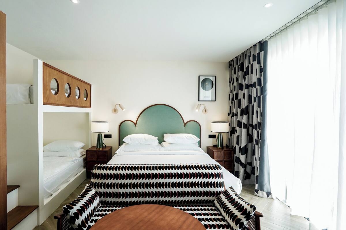 Une chambre d’hôtel avec un lit, une armoire en bois, une table de chevet, une lampe et un rideau à motifs.