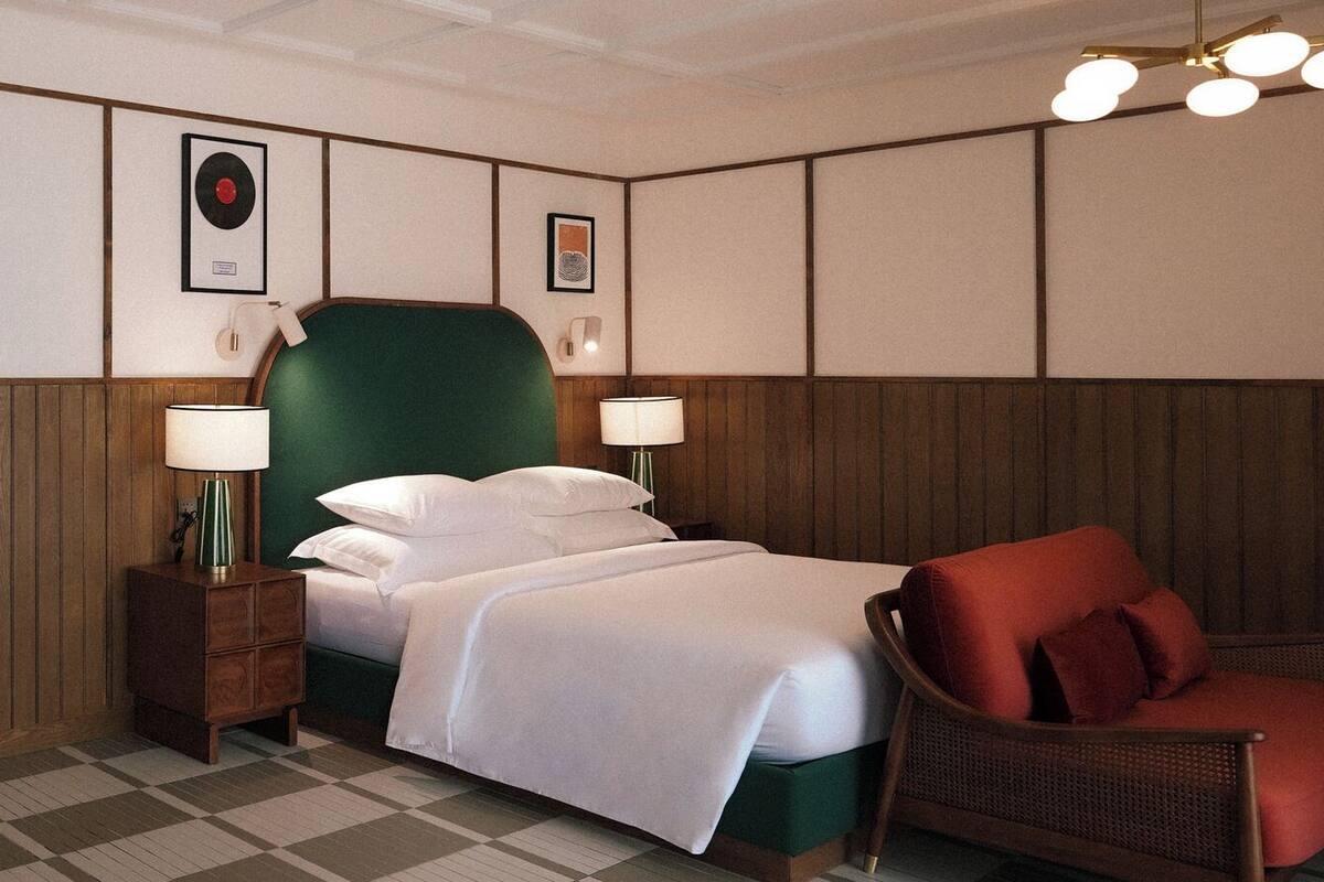 Une chambre d’hôtel comprenant un lit, deux lampes de chevet, une chaise et un luminaire fixé au mur.