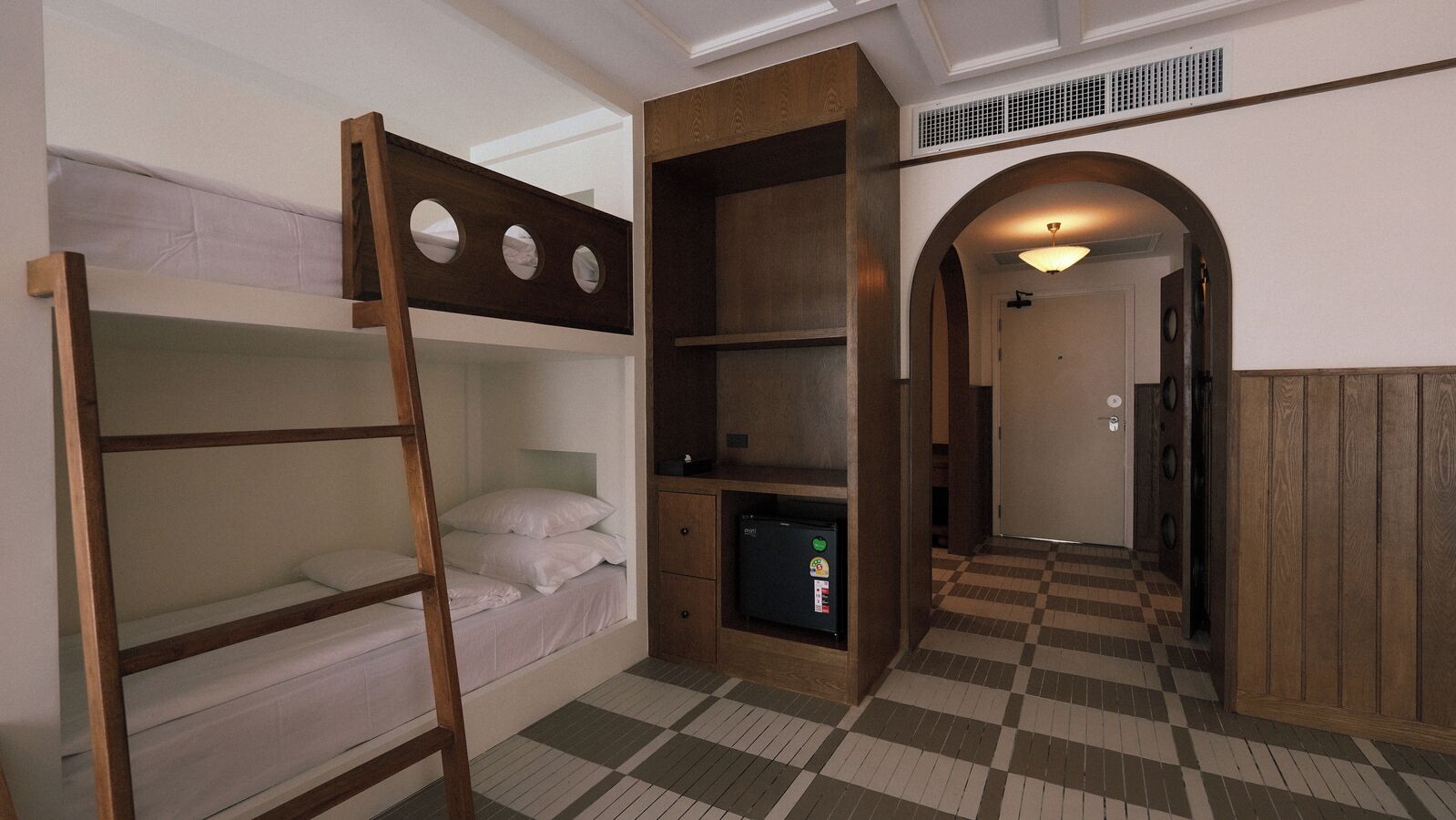 A room with bunk beds, a small refrigerator, and a checkered floor.
