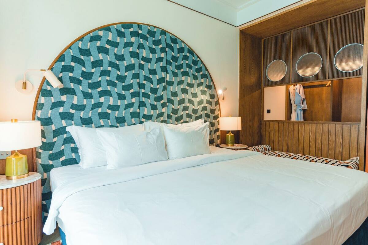 Un lit doté d’une grande tête de lit à motifs, de deux lampes de chevet et d’un mur en panneaux de bois orné de miroirs ronds.