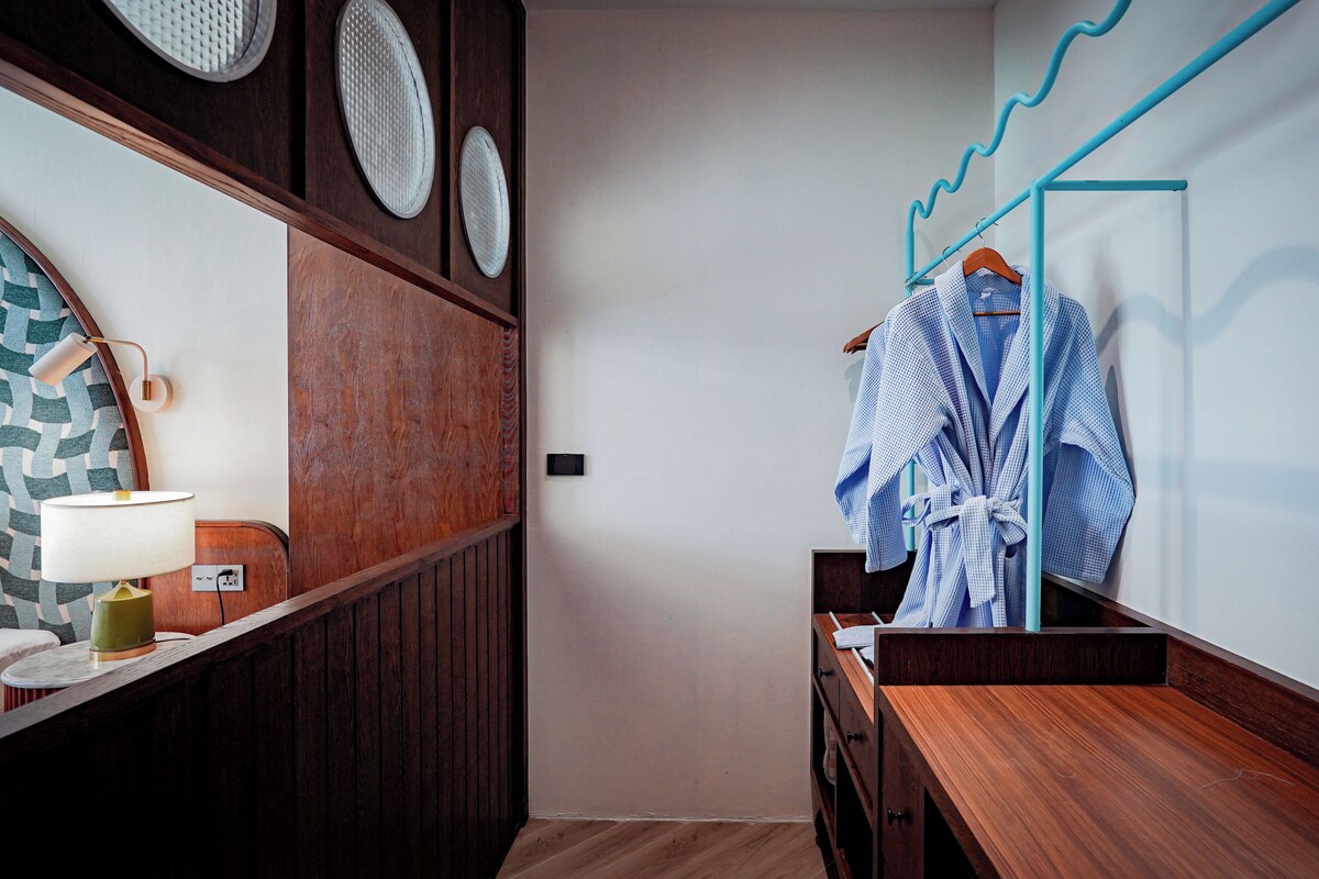 A bathroom with a wooden vanity, a mirror, a towel rack, and a robe hanging on the wall.