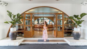 Une femme vêtue d’une robe rose se tient à l’entrée d’un bâtiment doté d’une arche en bois et de portes en verre.
