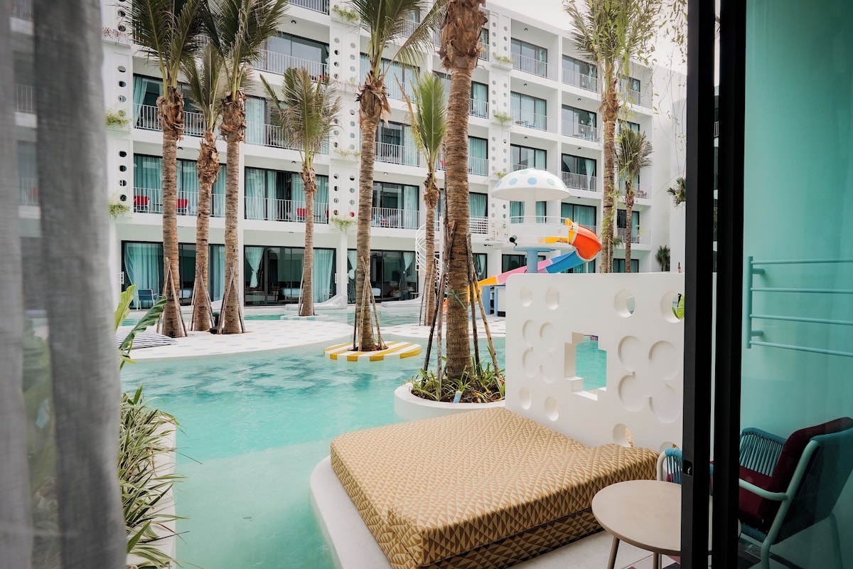 Quarto de hotel moderno com vista para uma área de piscina, incluindo palmeiras e um toboágua.
