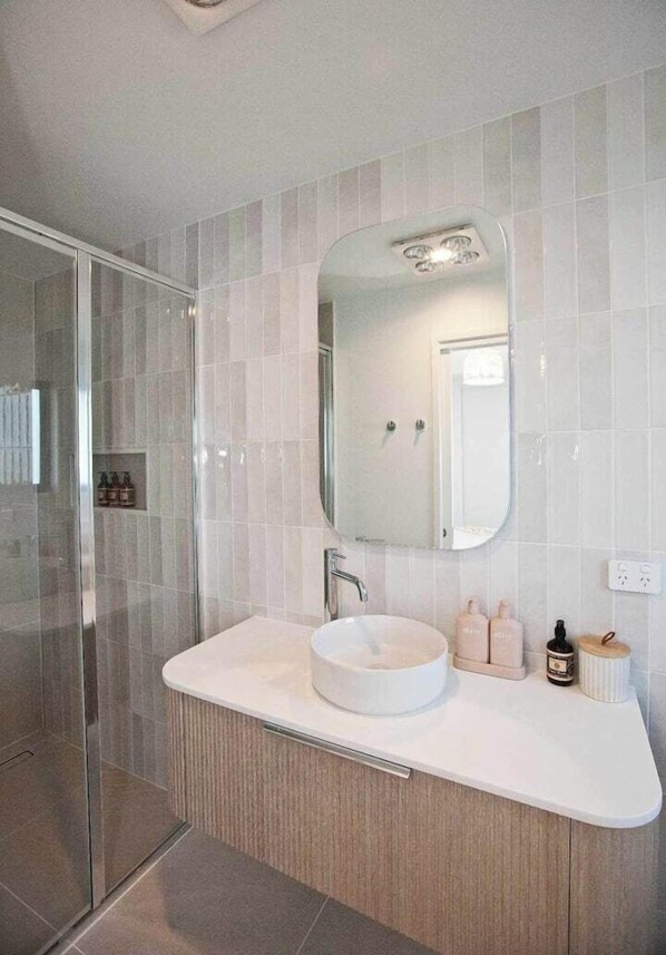 Un baño moderno con cabina de ducha de vidrio, lavamanos blanco y espejo grande.