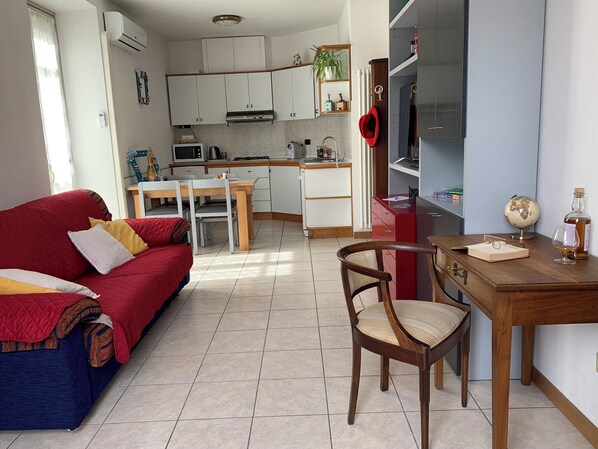 Un espacio habitable compacto con un sofá rojo, una mesa de comedor de madera con sillas, una zona de cocina con armarios blancos y un mueble rojo, y un globo en un estante.