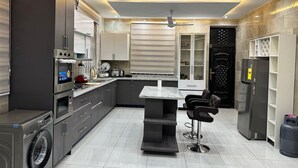 A modern kitchen with built-in appliances, a central island, bar stools, and a black refrigerator. - Nanani Luxury Villa - Kumasi (Kumasi)