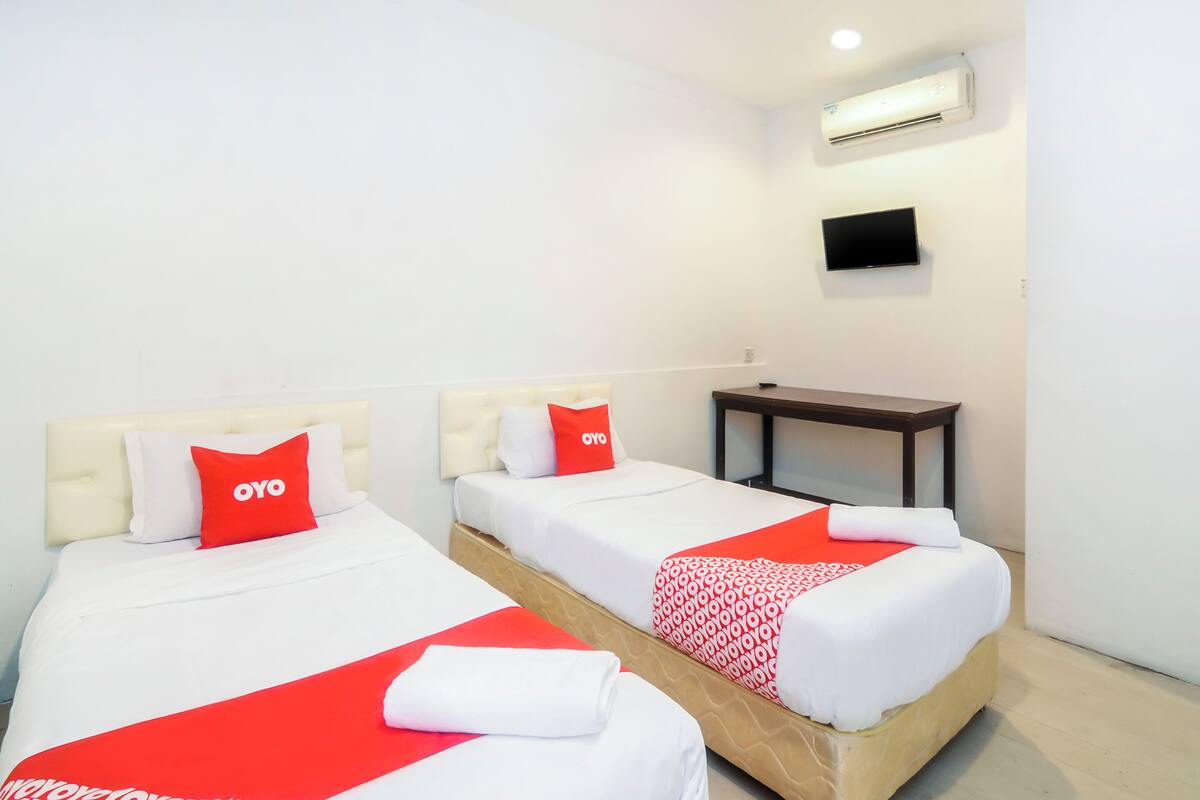 Une chambre d’hôtel avec deux lits, chacun agrémenté de draps blancs et de touches de couleur rouge, une petite table et un téléviseur fixé au mur.