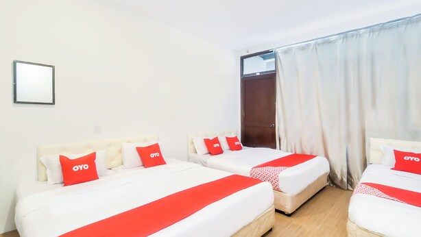 A hotel room with three beds, each with white bedding and red accents. There is a window with white curtains and a door visible. - OYO 44017 L & C Premium Stay  (Kuching)
