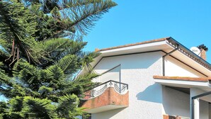Una casa moderna con fachada blanca, un balcón y un gran árbol en primer plano.