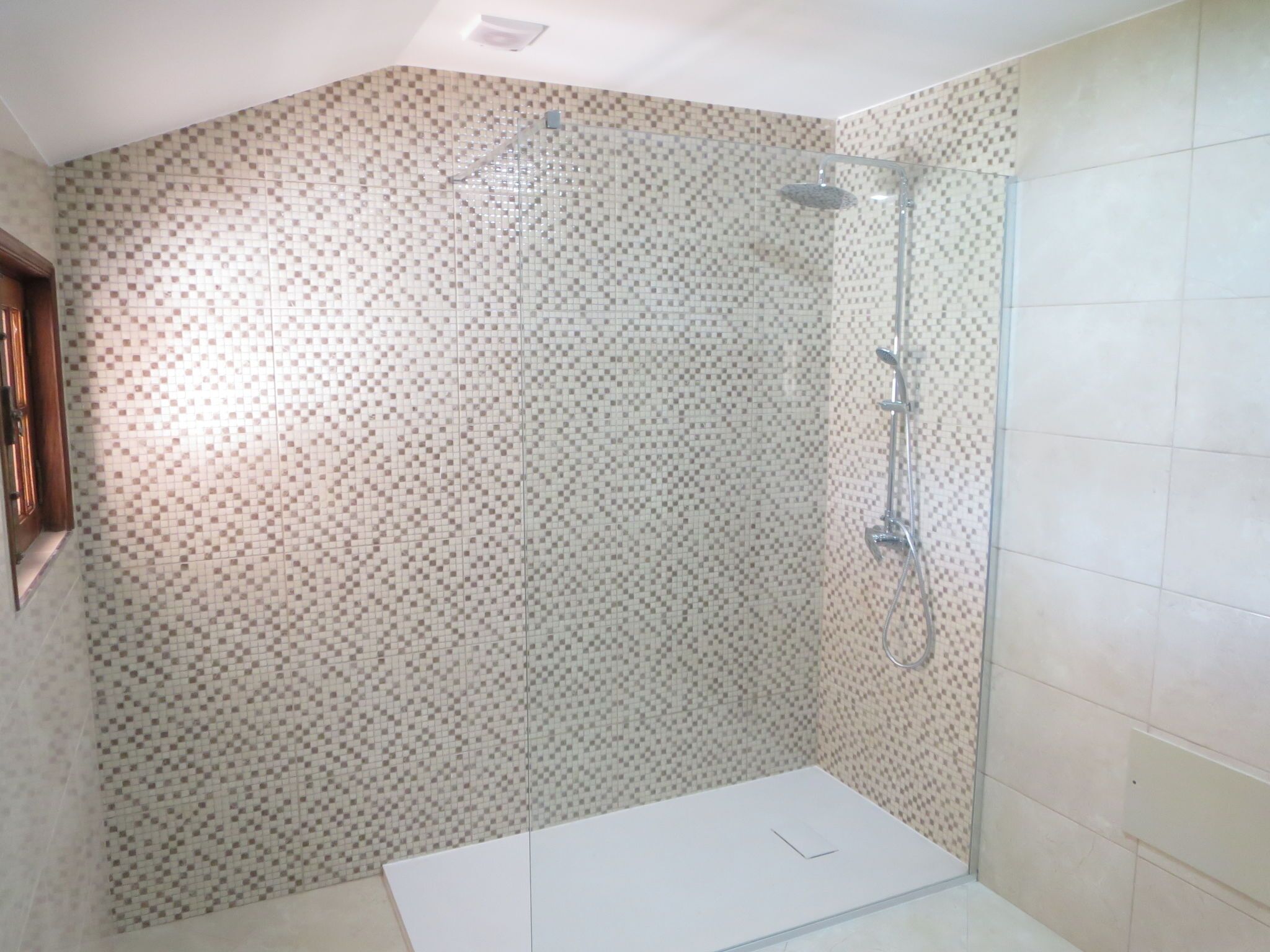 A shower area with a glass door, tiled walls, and a white floor.