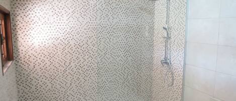 A shower area with a glass door, tiled walls, and a white floor.