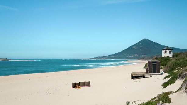 Ein Strand mit einem kleinen weißen Gebäude, einer Holzbank und einem Geländewagen.