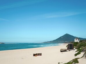 A beach with a small white building, a wooden bench, and a dune buggy.