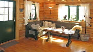 A cozy log cabin interior with a sofa, a coffee table, and a window with curtains.