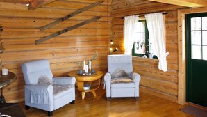 A cozy log cabin room with two armchairs, a small round table, and a window with curtains.