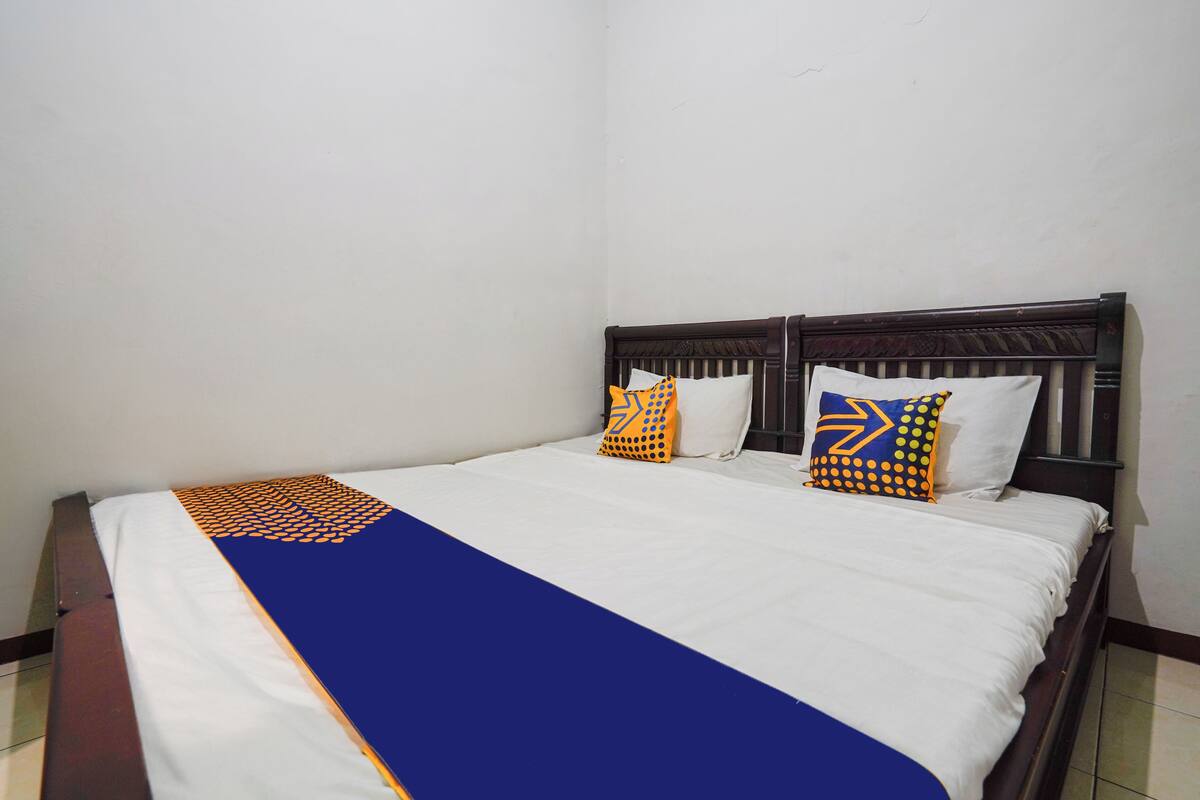 Un lit bien fait, recouvert d’une couvre-lit bleue et blanche, agrémenté de deux coussins à motifs et doté d’une tête de lit en bois.
