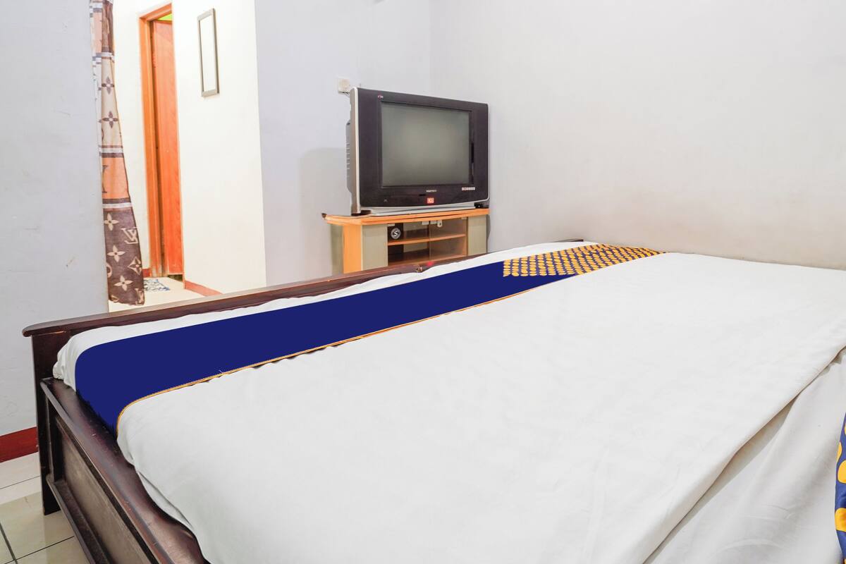 Un lit recouvert d’une couvre-lit bleue et blanche, un téléviseur posé sur un meuble en bois et un rideau à motifs.