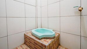 Une petite salle de bain avec des toilettes bleues, des murs carrelés et un pommeau de douche.