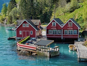 A red wooden house with a dock, a boat, and a forested hillside. - Jambueggi by Interhome (Arnafjord)