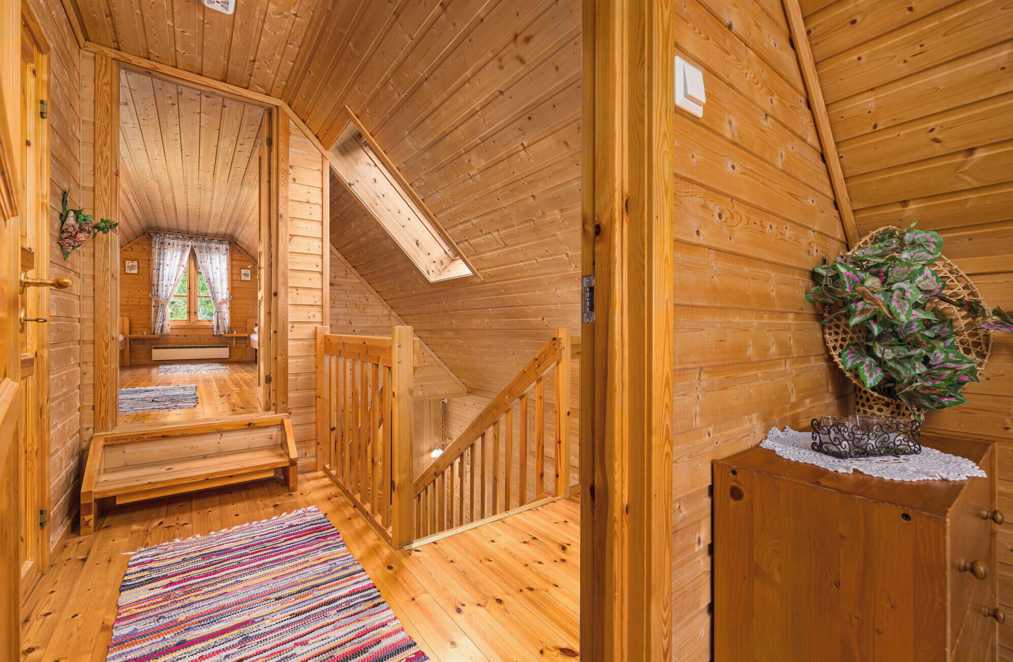 Un intérieur en bois avec un escalier, un banc, une plante et une fenêtre avec des rideaux.