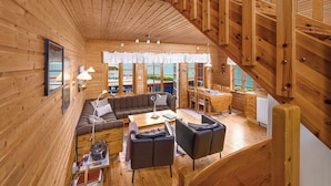 Ein Holzblockhaus mit Schlafempse, Essbereich im Obergeschoss, einer Couch und einem Couchtisch.