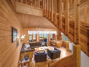 A wooden cabin interior with a loft dining area, a sofa, and a coffee table.