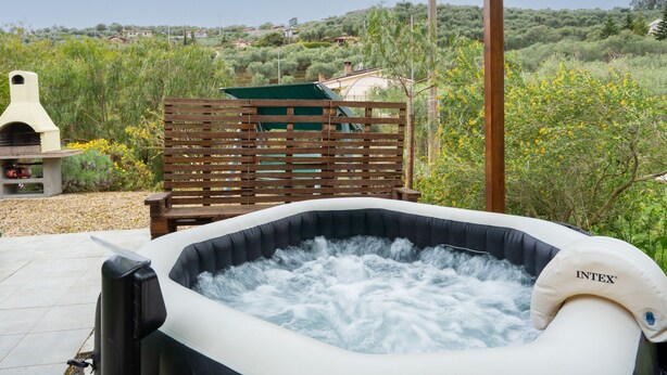 Un bain à remous avec vue sur un paysage rural, une terrasse en bois et un barbecue.