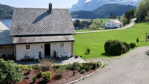 A house with a sloped roof and a chimney, a paved driveway, and a well-maintained garden with a bench and chairs.