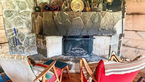 A stone fireplace with a fire, surrounded by wooden chairs and a woven rug. - Haukedalspanorama by Interhome (Haukedalsvatn)