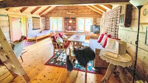 A cozy log cabin interior with a high ceiling, wooden floors, a dining area, and a living room with a sofa and chairs. - Haukedalspanorama by Interhome (Haukedalsvatn)