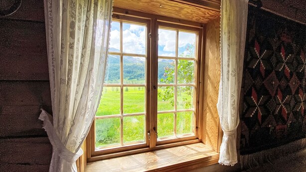 A wooden cabin with a large window, curtains, and a view of a green landscape. - Haukedalspanorama by Interhome (Haukedalsvatn)