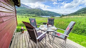 A wooden deck with a table and chairs, overlooking a green field and mountains. - Haukedalspanorama by Interhome (Haukedalsvatn)